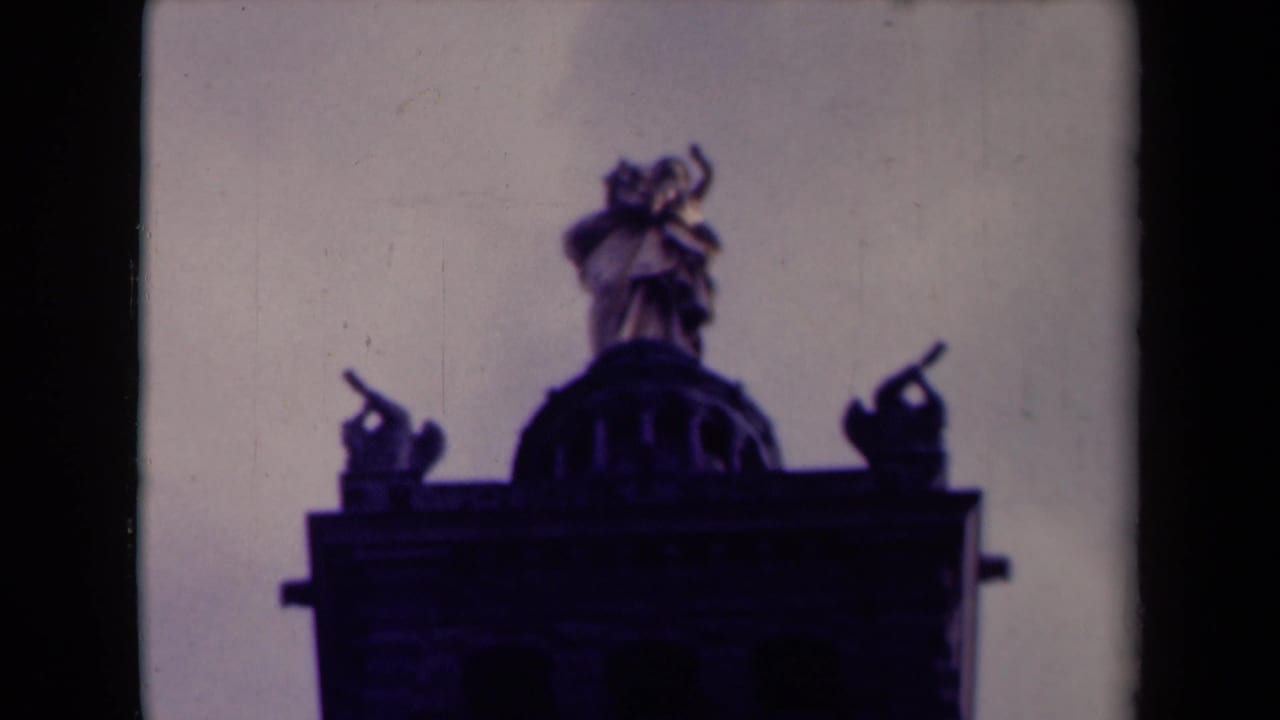 Rooftop sculptural group with flanking figures silhouetted above a building facade.