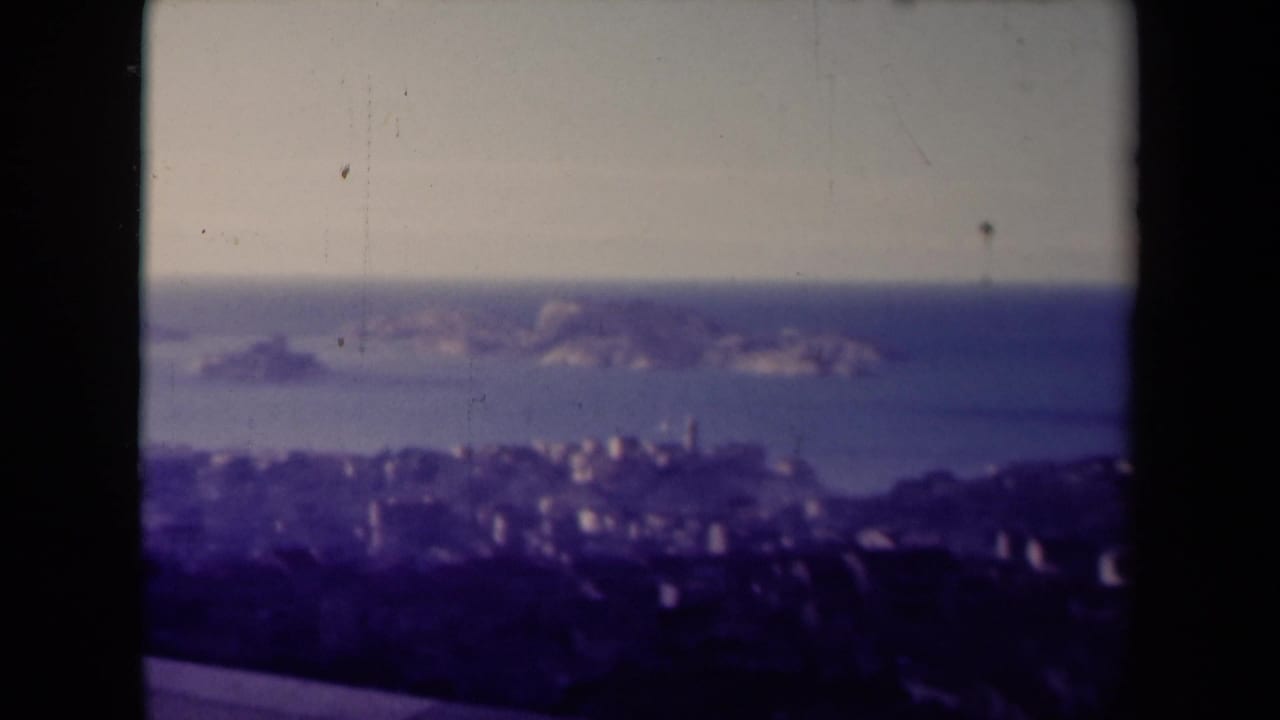 Soft coastal panorama with rocky islands offshore and a hazy city shoreline below.
