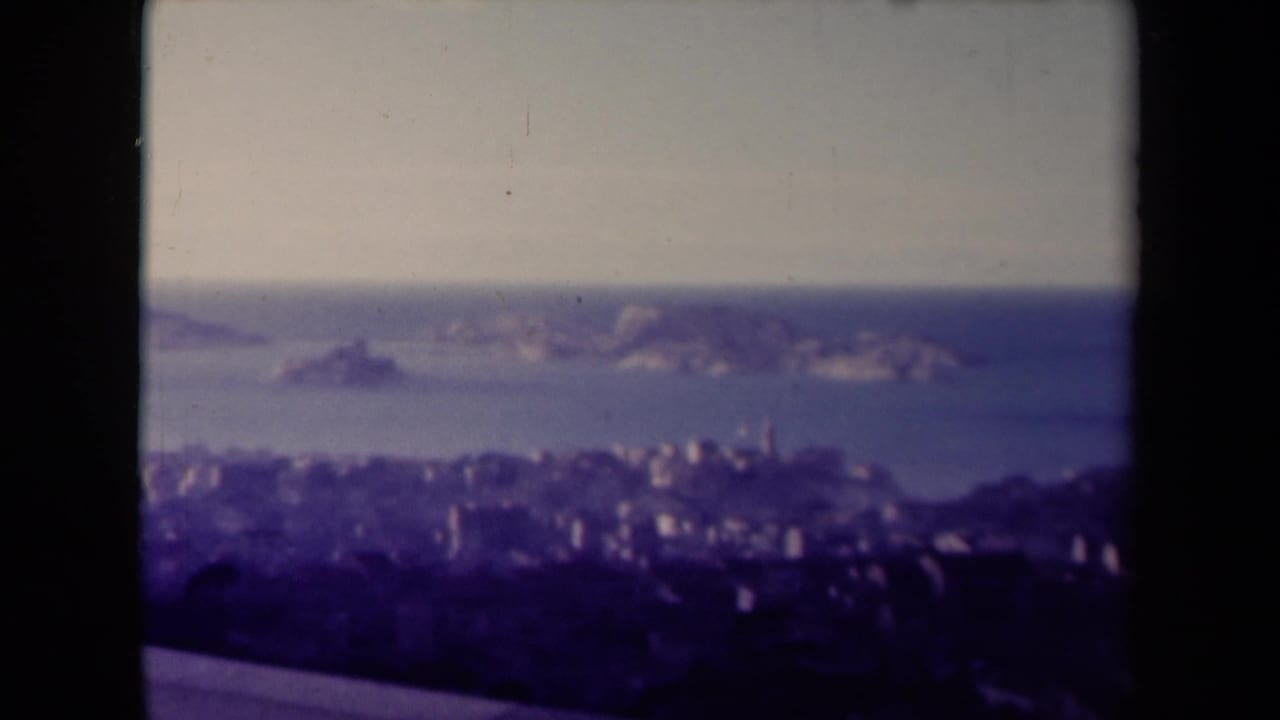 Distant shoreline city with offshore rocks and sea, framed by dark film gate edges.