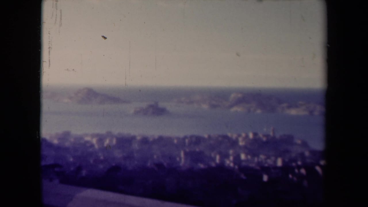 Final 1945 France frame holding on a hazy coastal panorama, with offshore rocks, shoreline buildings, and 8mm gate borders.
