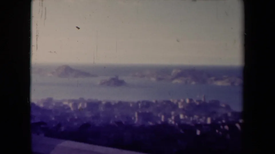 Final 1945 France frame holding on a hazy coastal panorama, with offshore rocks, shoreline buildings, and 8mm gate borders.