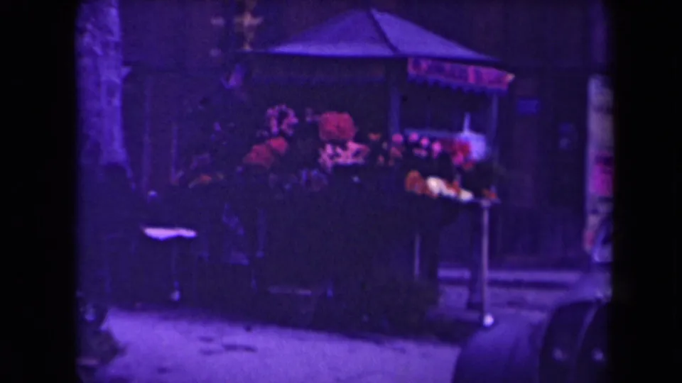 1945 France frame with a small outdoor stall under a canopy, rendered in soft purple-shifted 8mm color.