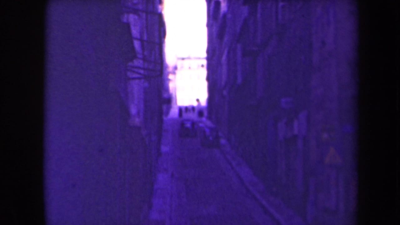1945 France frame looking down a dim urban alley toward a bright opening with distant people silhouetted.