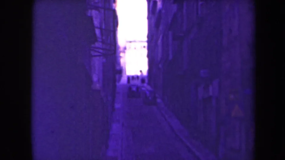 1945 France frame looking down a dim urban alley toward a bright opening with distant people silhouetted.