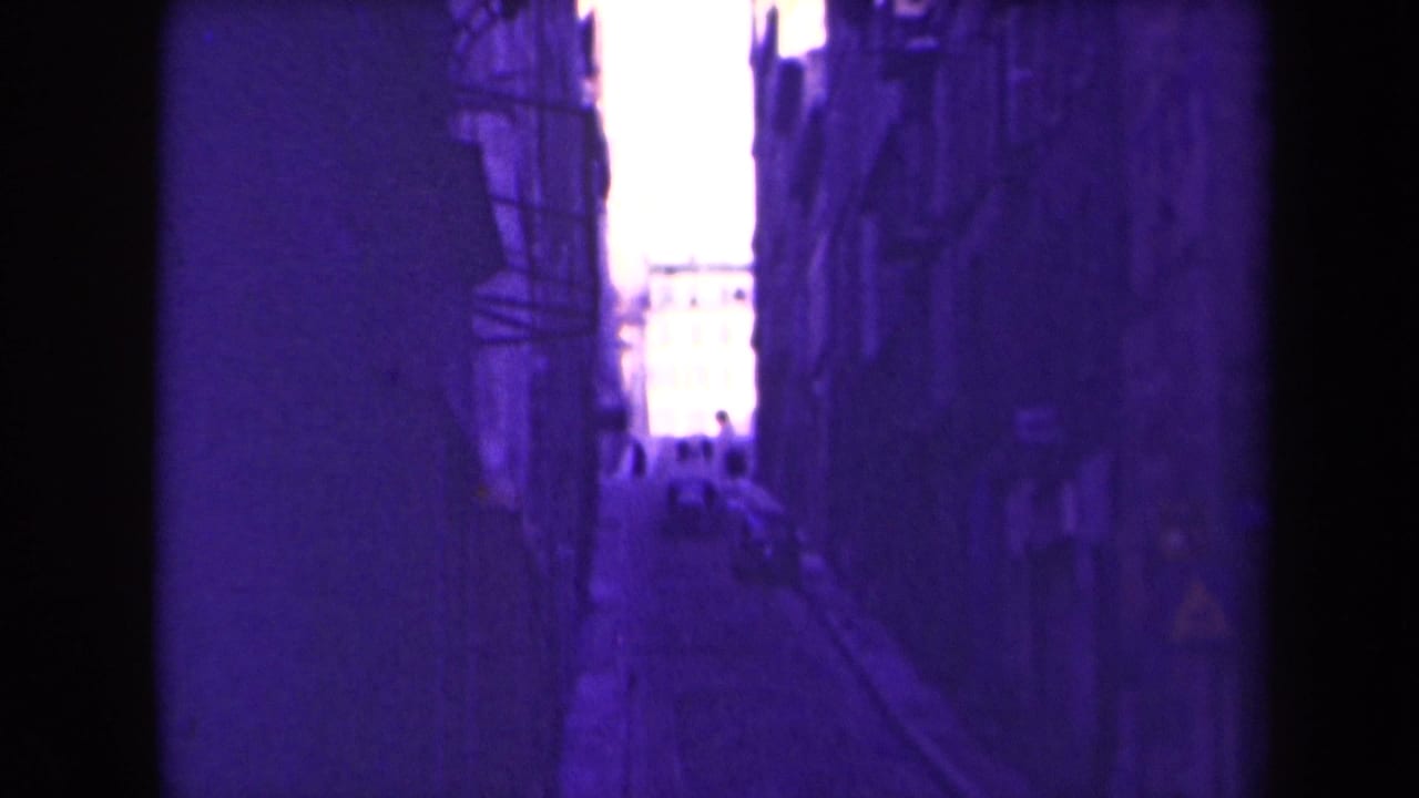 Narrow alleyway between dark building walls with a bright opening at the far end.