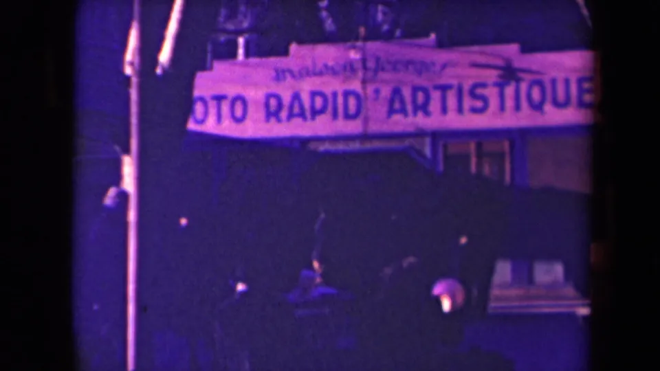 1940s France frame with a prominent PHOTO RAPID ARTISTIQUE sign over a dim street scene with pedestrians.