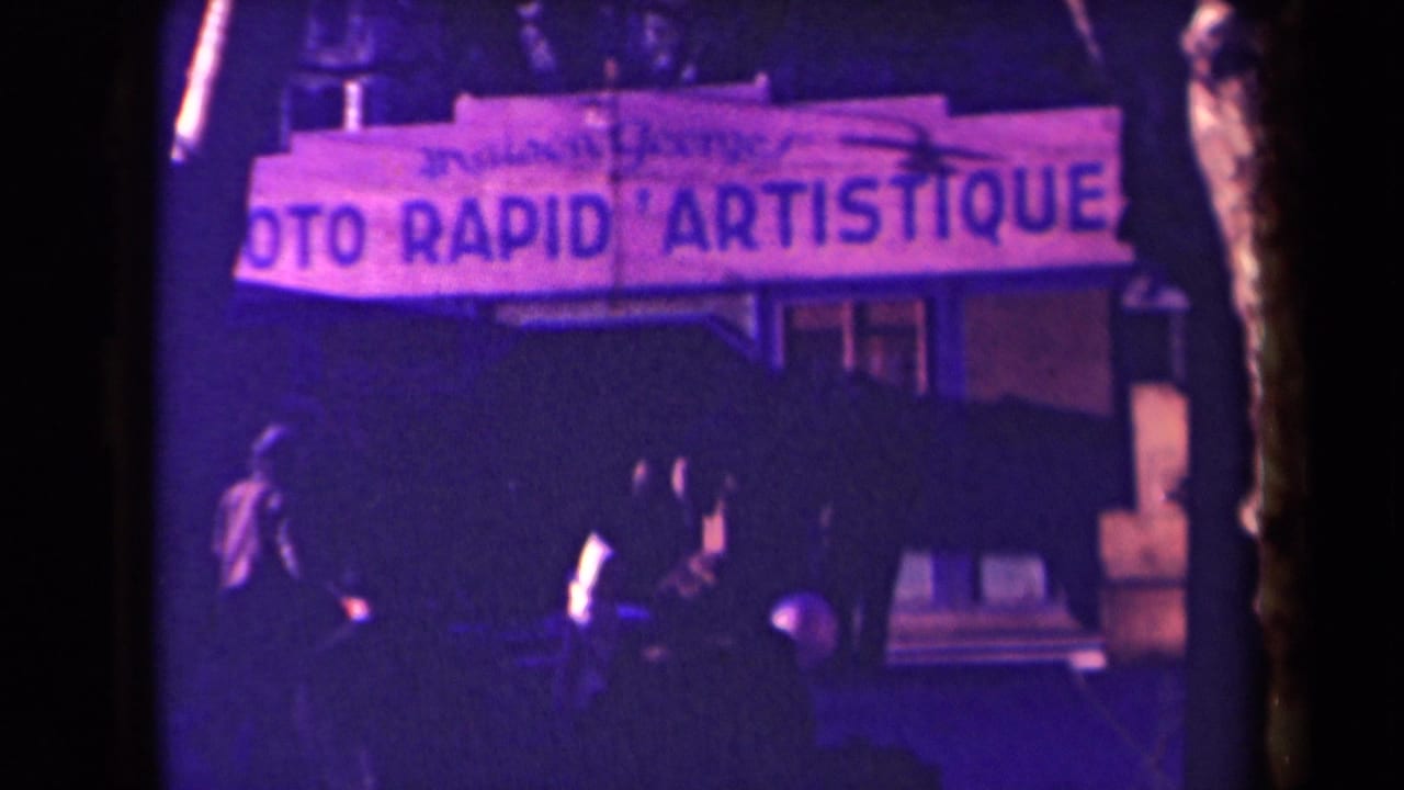 1940s France home-movie frame focused on the PHOTO RAPID ARTISTIQUE sign above a dim sidewalk crowd.