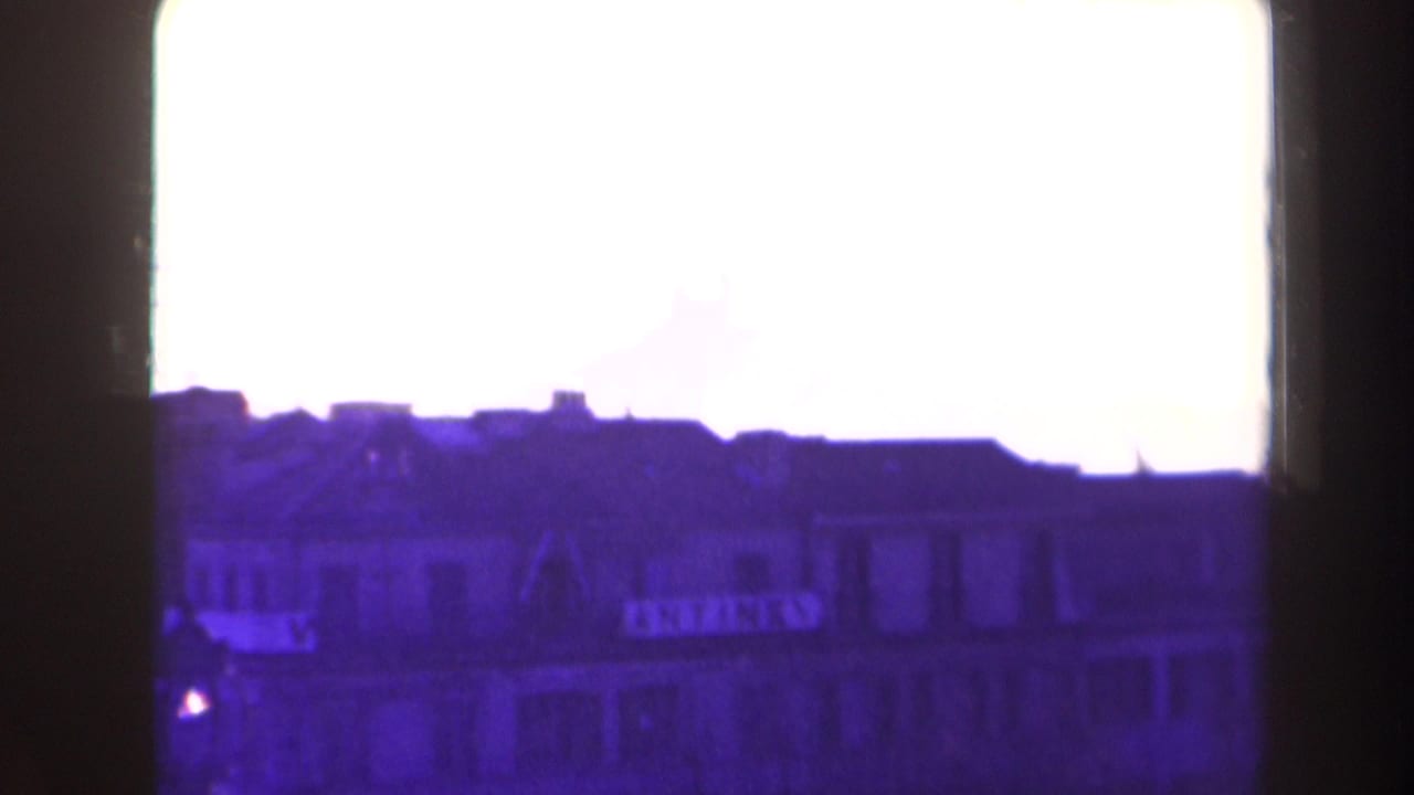 Overexposed 1940s France home-movie frame showing a city roofline and building facades in silhouette.