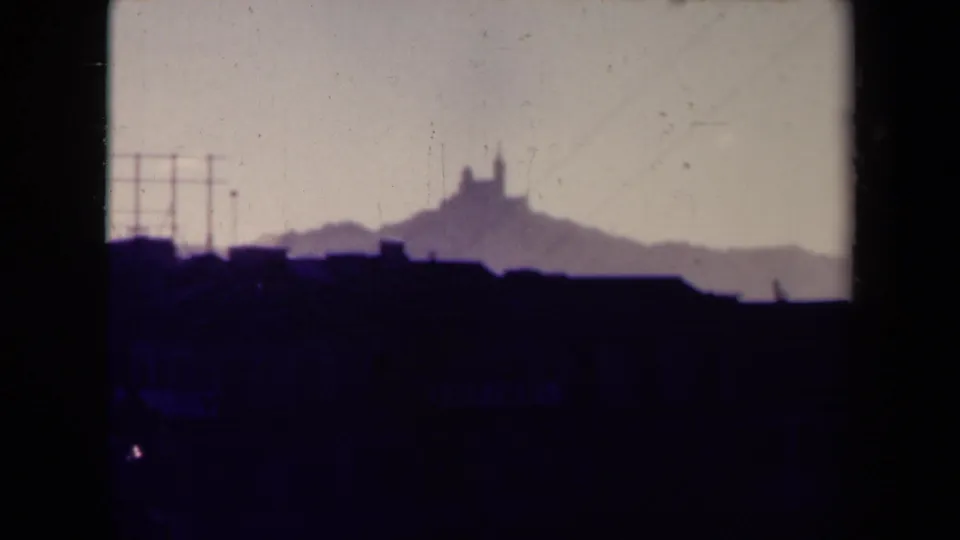 1945 France 8mm view of dark rooftops and a distant hilltop silhouette softened by haze and film grain.