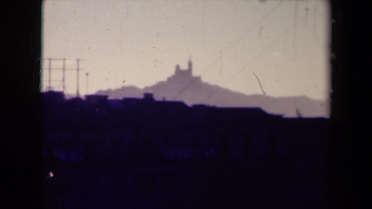 1945 France 8mm frame with a distant hilltop landmark, rooftop silhouettes, pale sky, and visible film wear.