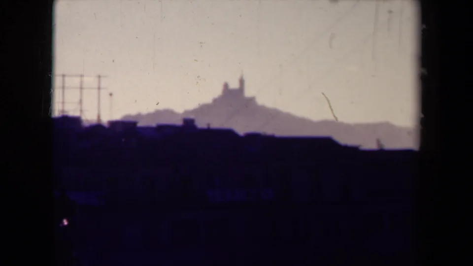 1945 France 8mm frame with a distant hilltop landmark, rooftop silhouettes, pale sky, and visible film wear.