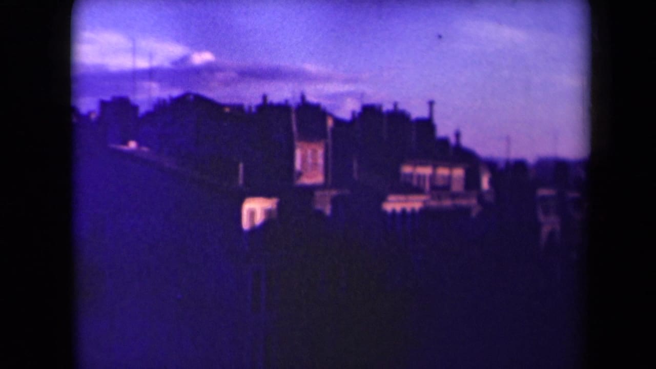 1945 France 8mm frame shifting closer to city buildings, with purple color cast, rooflines, and bright window areas.