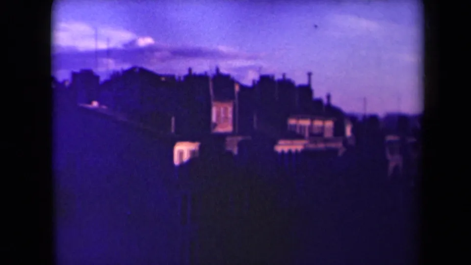 1945 France 8mm frame shifting closer to city buildings, with purple color cast, rooflines, and bright window areas.