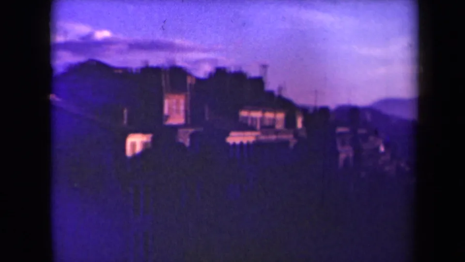 1945 France home-movie frame showing a soft, purple-toned cityscape at dusk with rooftops, hills, and dark foreground silhouettes.