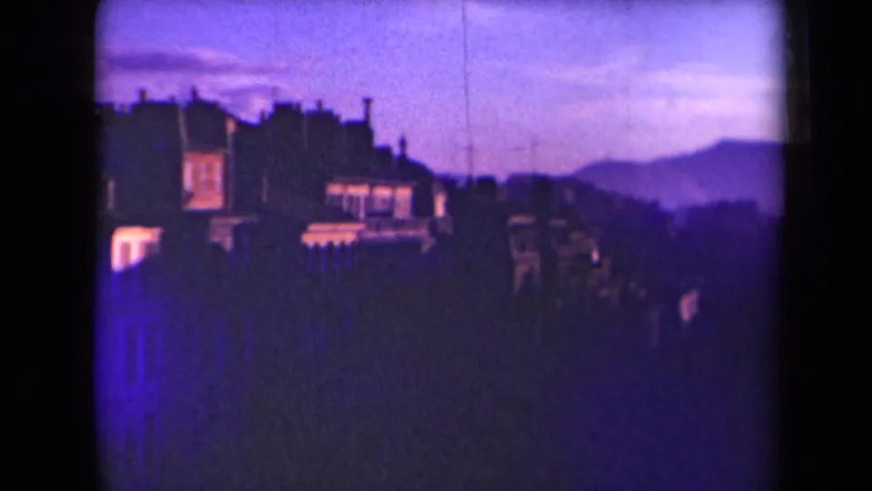 1945 France frame with silhouetted urban buildings and distant hills under a purple twilight sky, bordered by the 8mm film gate.