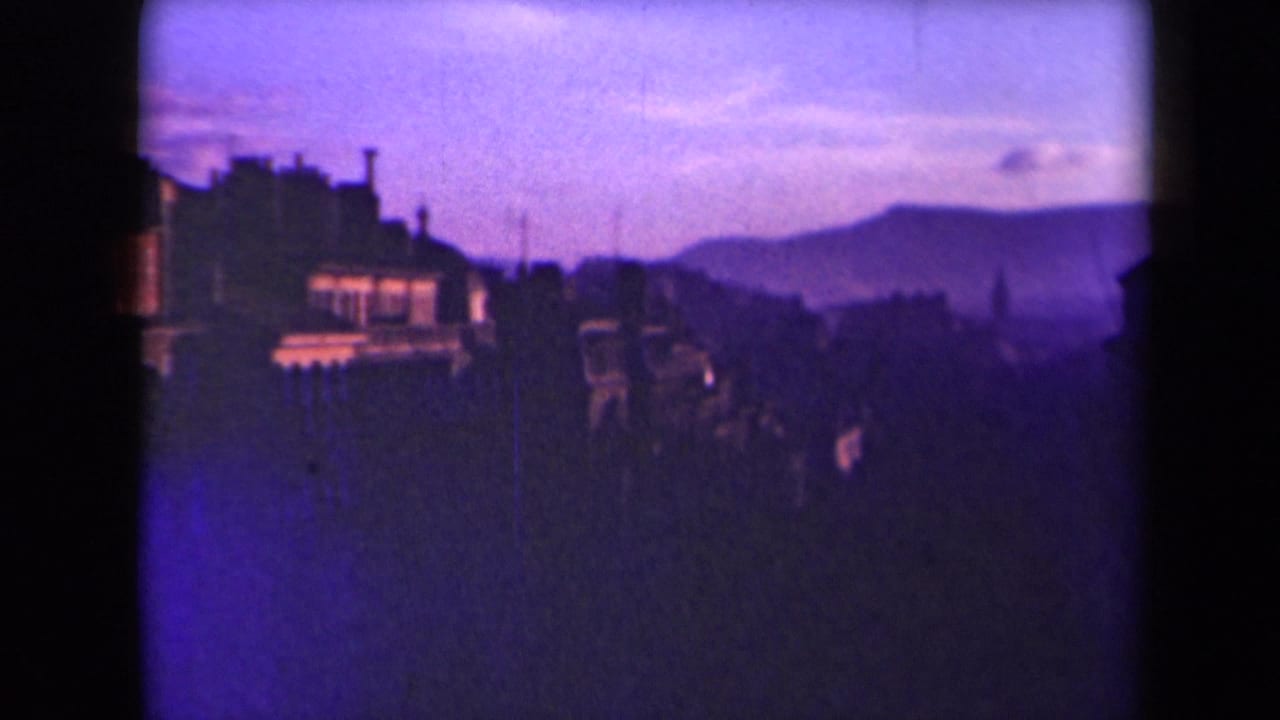 1945 France home-movie view of rooftops and a hazy hillside skyline, with heavy purple-blue color shift and darkened foreground.