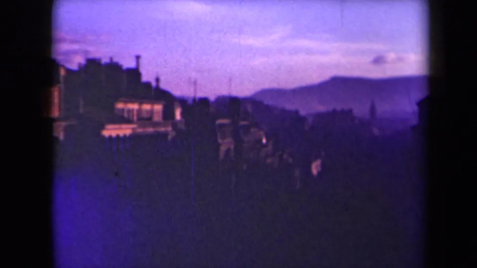 1945 France home-movie view of rooftops and a hazy hillside skyline, with heavy purple-blue color shift and darkened foreground.