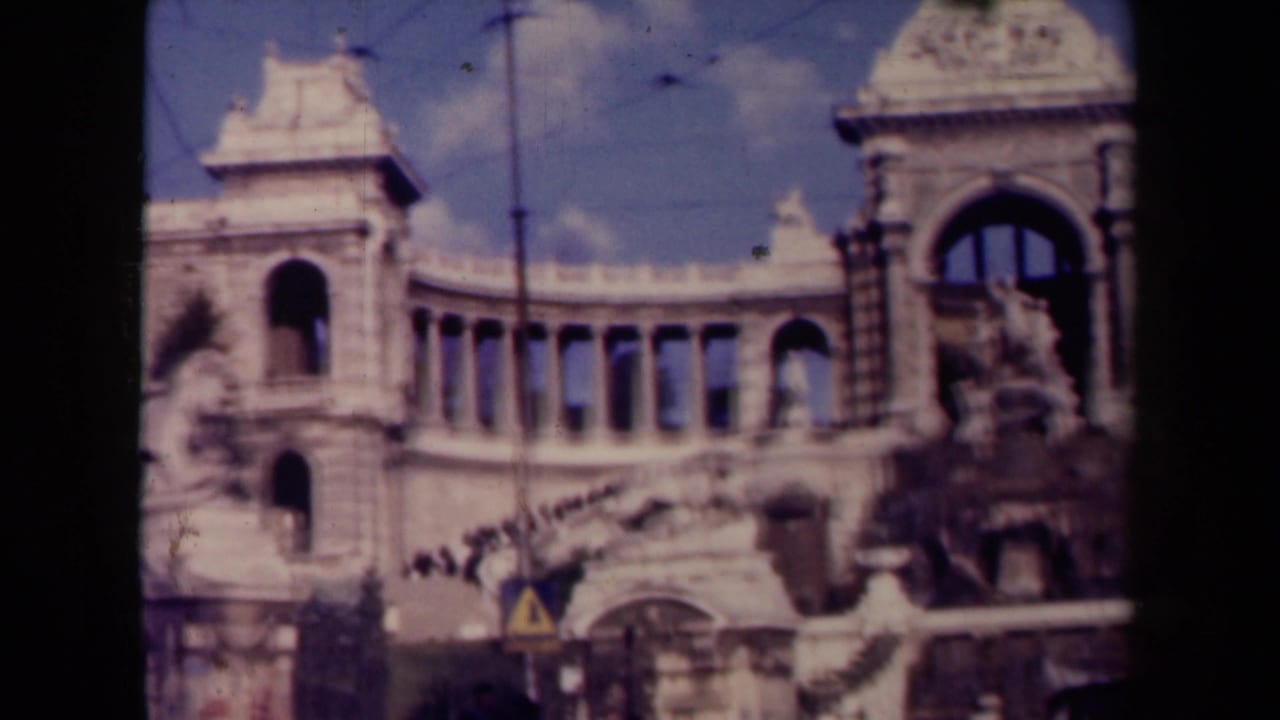 Visitor-shot 1940s view of the Palais Longchamps exterior, with classical columns, arched windows, statues, and bright sky.