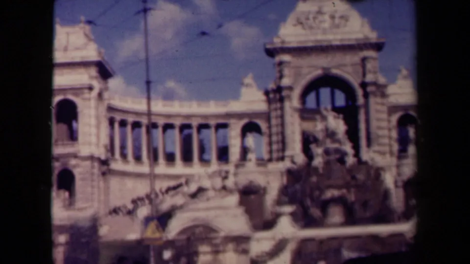 1945 France 8mm frame showing an ornate stone facade with arched windows, sculptural detail, overhead wires, and bright sky.