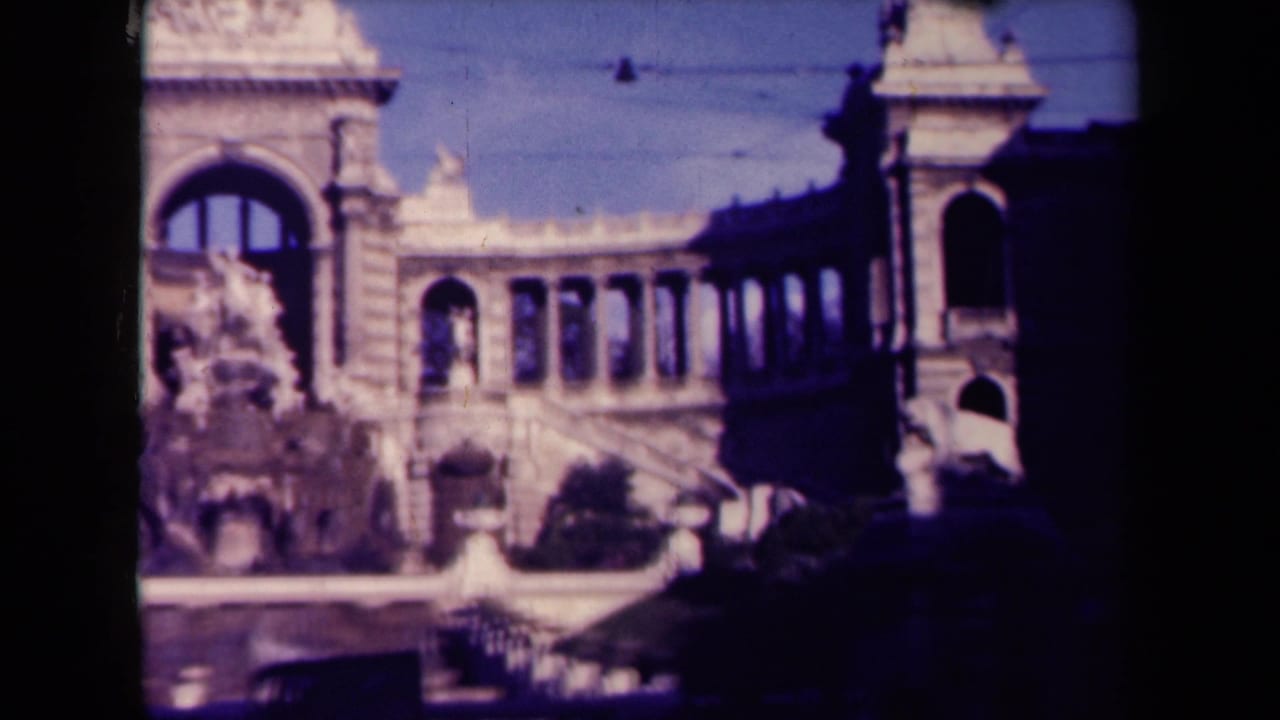 Soft 8mm frame of an ornate fountain before a classical stone building with arches.