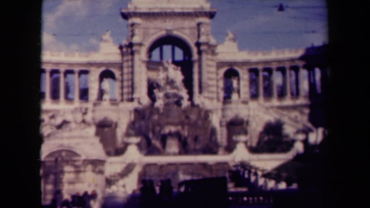 Arched stone landmark with columns, fountain sculpture, overhead wires, and a dark vehicle at street level.