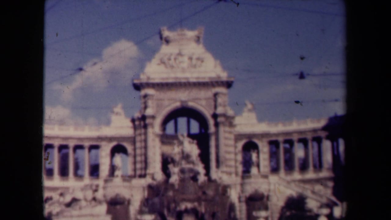 1940s France frame of a grand arched public landmark seen in soft 8mm color with overhead wires crossing the sky.