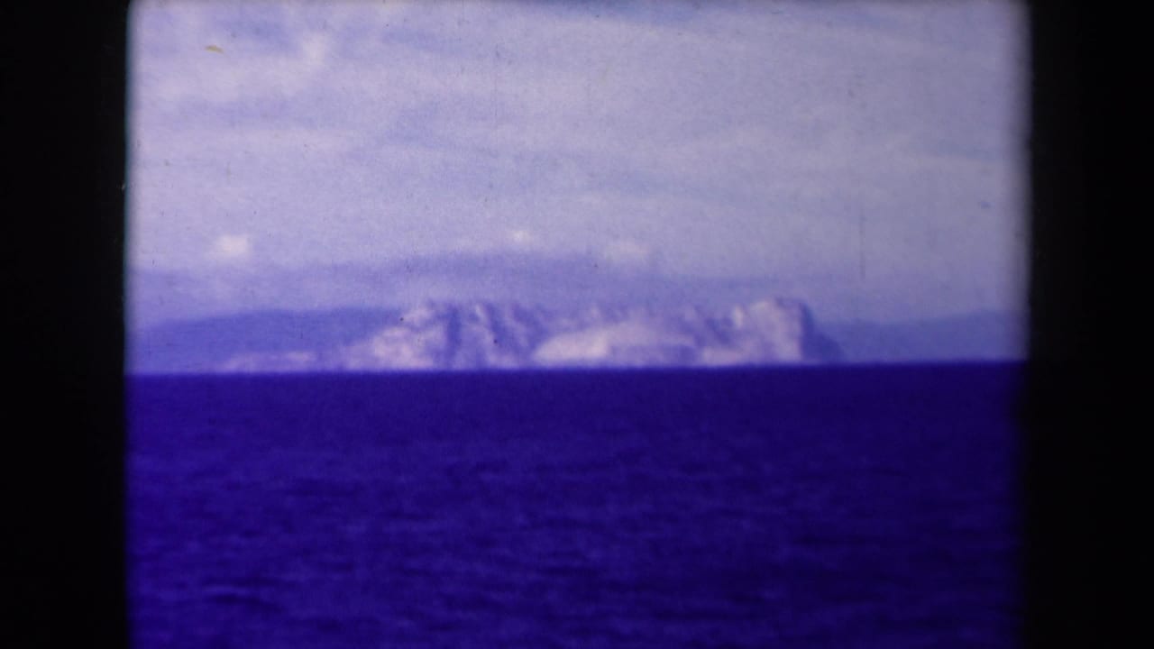 Distant pale mountains across a dark blue sea under a cloudy sky.