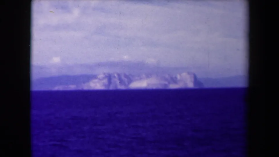 1945 8mm France footage shows a hazy mountain range beyond open water beneath layered cloud, with visible film borders and color shift.