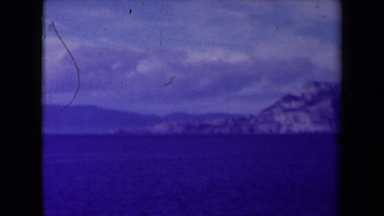 Distant snowy cliff coastline across dark blue water under a clouded sky.
