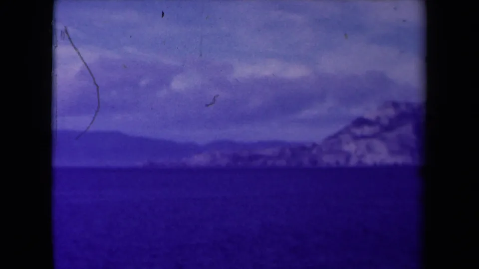 1945 France 8mm frame showing a distant snow-covered cliff coast across dark water with a purple-blue film cast.