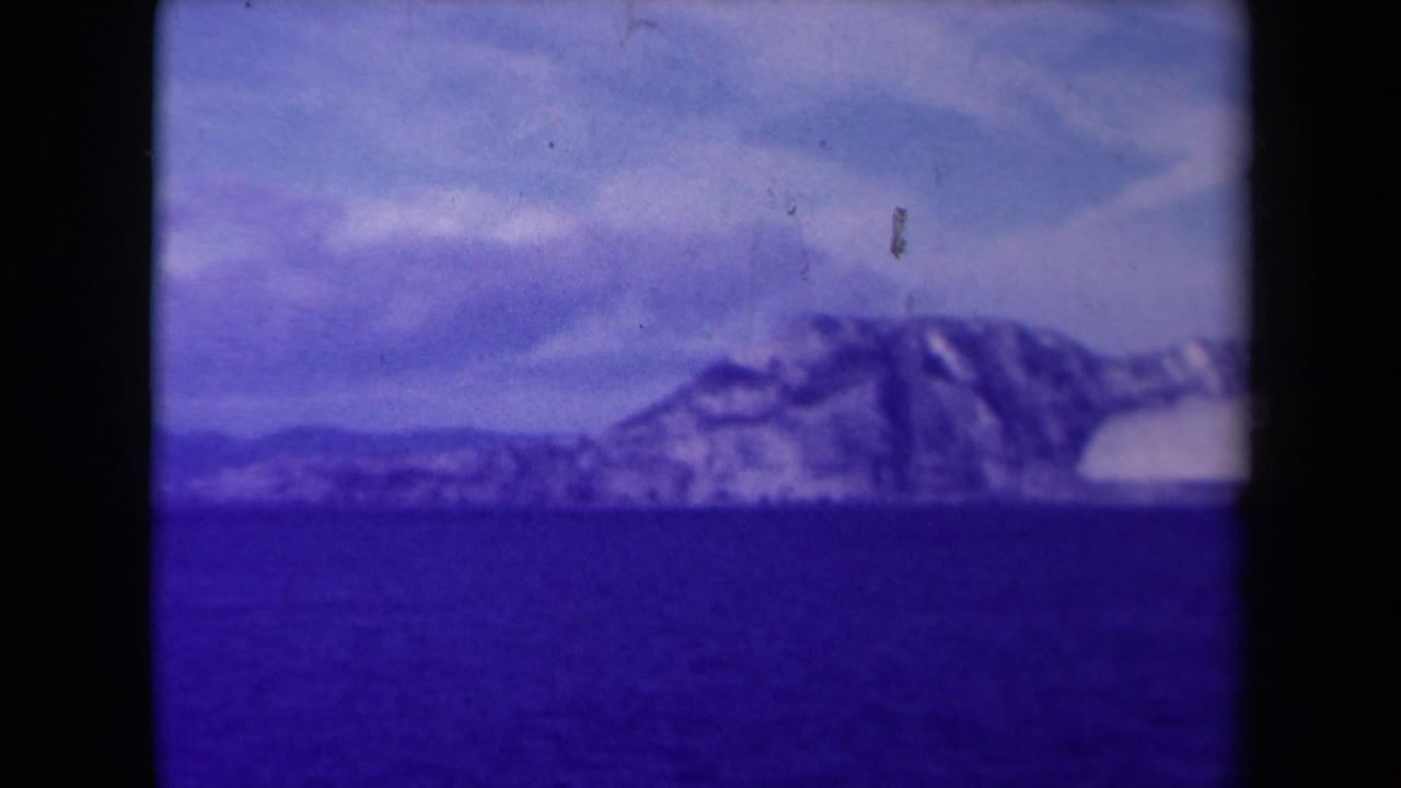 1945 France 8mm frame of snowy coastal cliffs over dark water, with pale clouds and visible film wear.