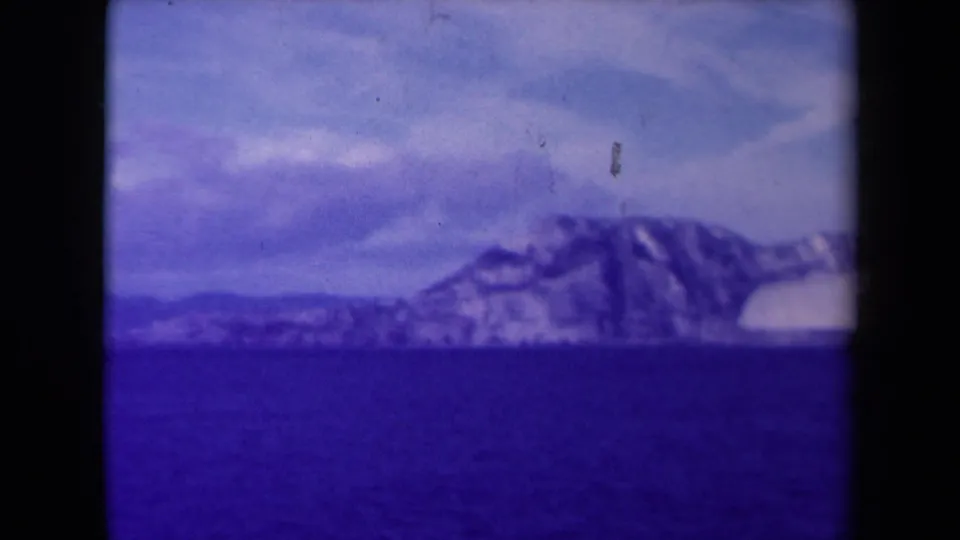 1945 France 8mm frame of snowy coastal cliffs over dark water, with pale clouds and visible film wear.