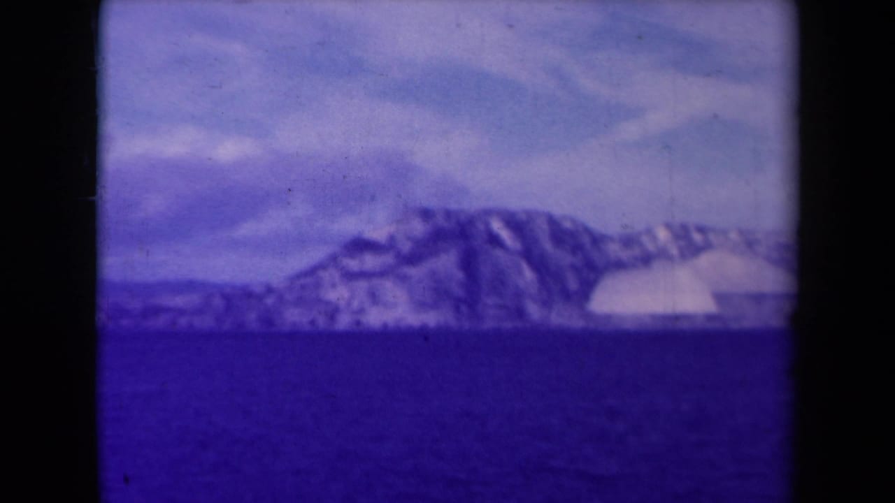 1945 France coastal landscape showing a snow-covered headland across water, recorded on soft, color-shifted 8mm film.