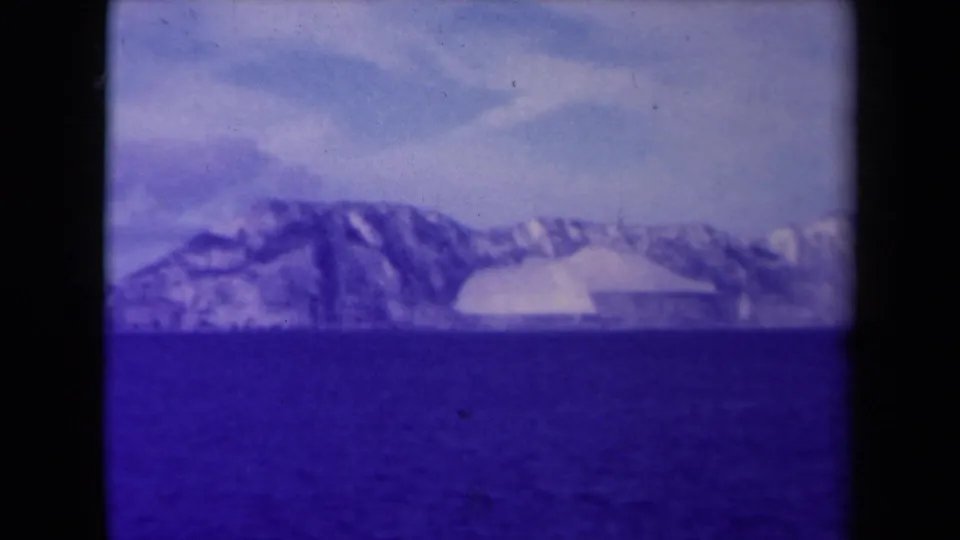 A soft 1945 France 8mm view of water and distant snow or ice-covered coastal landforms, with visible film grain and frame edges.