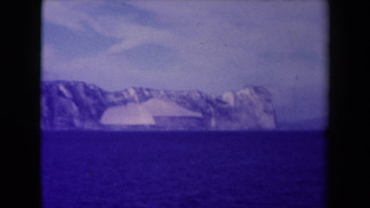 End frame of a 1945 France 8mm coastal view, with a glacier-like shoreline across the water and strong blue-purple film cast.