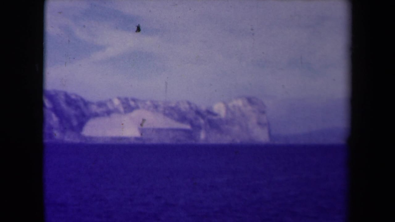 Distant glacier or ice mass across blue water under a pale sky.