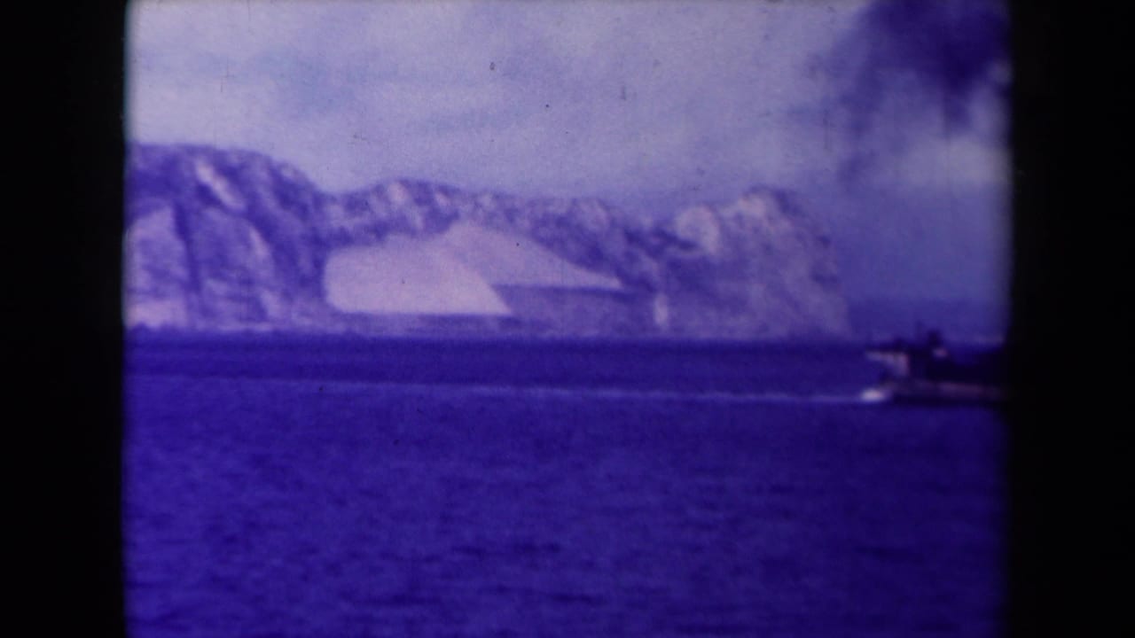 The distant steamship moves out of frame to the right, leaving smoke over blue water and a glacier-like coast in the background.