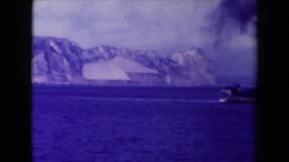 The distant steamship moves out of frame to the right, leaving smoke over blue water and a glacier-like coast in the background.