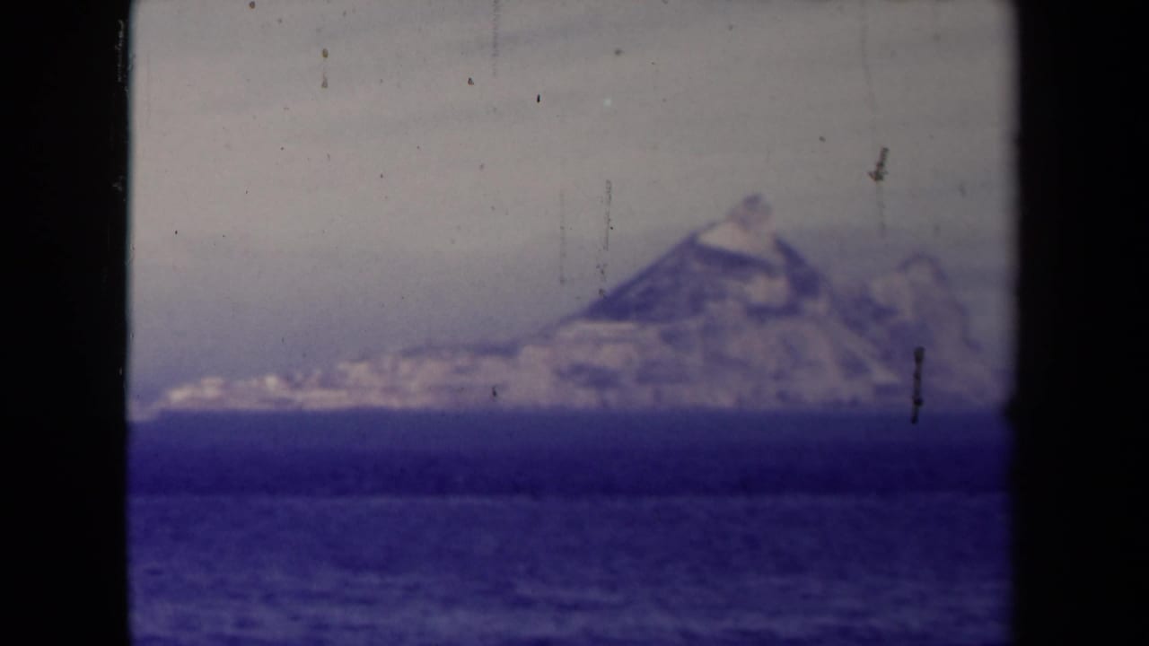 1945 France-labeled 8mm still showing a distant rugged formation above the ocean, tinted blue and softened by age.