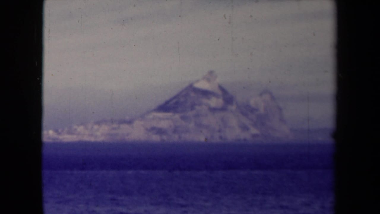 France-labeled 1945 frame showing a hazy coastal or iceberg-like formation across rippled blue water with aged 8mm texture.