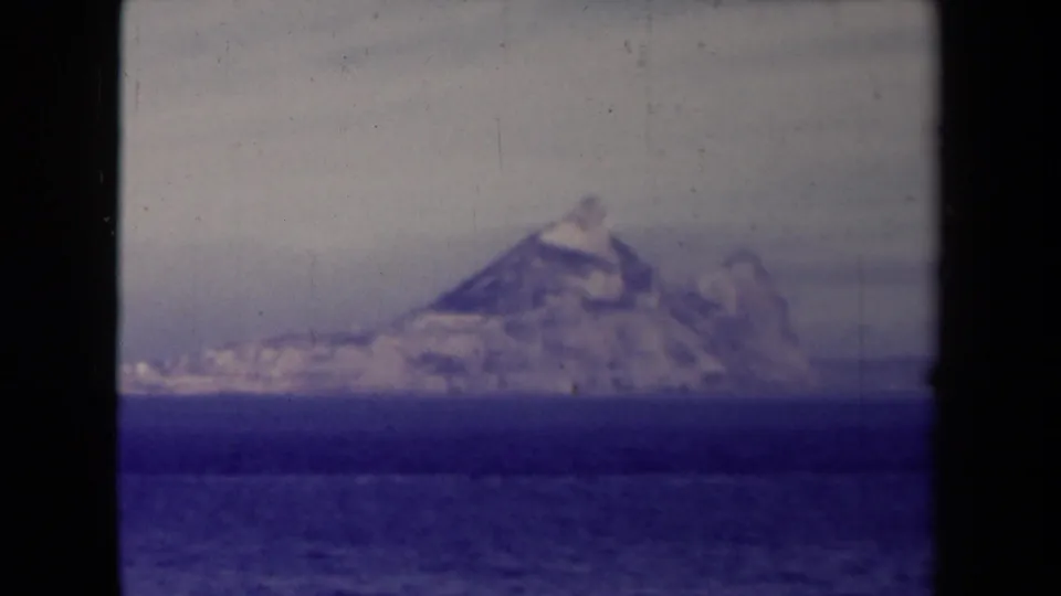 France-labeled 1945 frame showing a hazy coastal or iceberg-like formation across rippled blue water with aged 8mm texture.