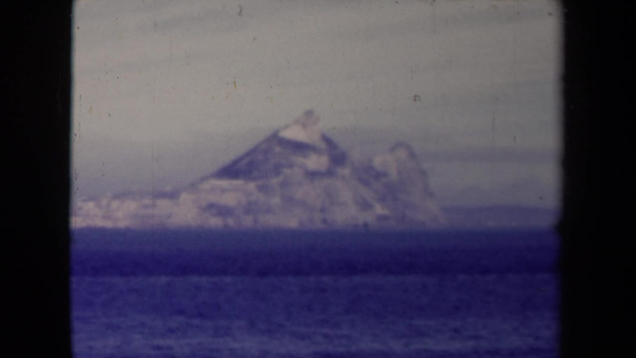 1945 8mm home-movie frame showing a distant rugged island or headland across blue ocean, partly bordered by dark film edges.