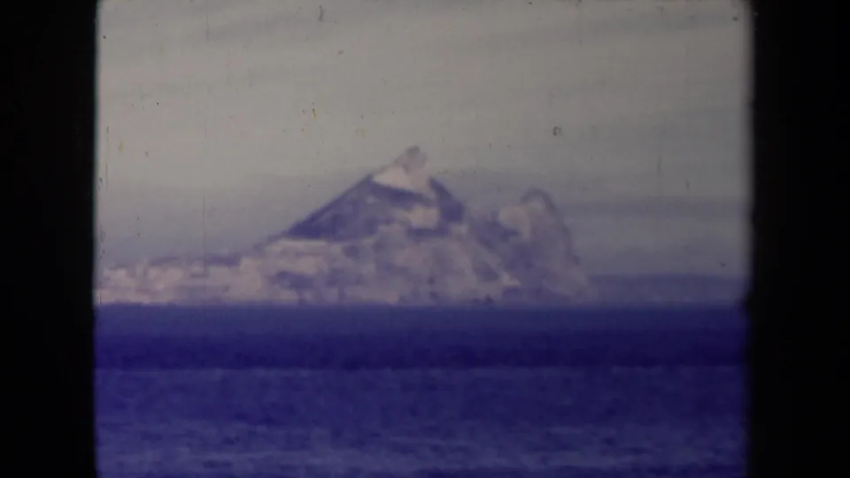 1945 8mm home-movie frame showing a distant rugged island or headland across blue ocean, partly bordered by dark film edges.
