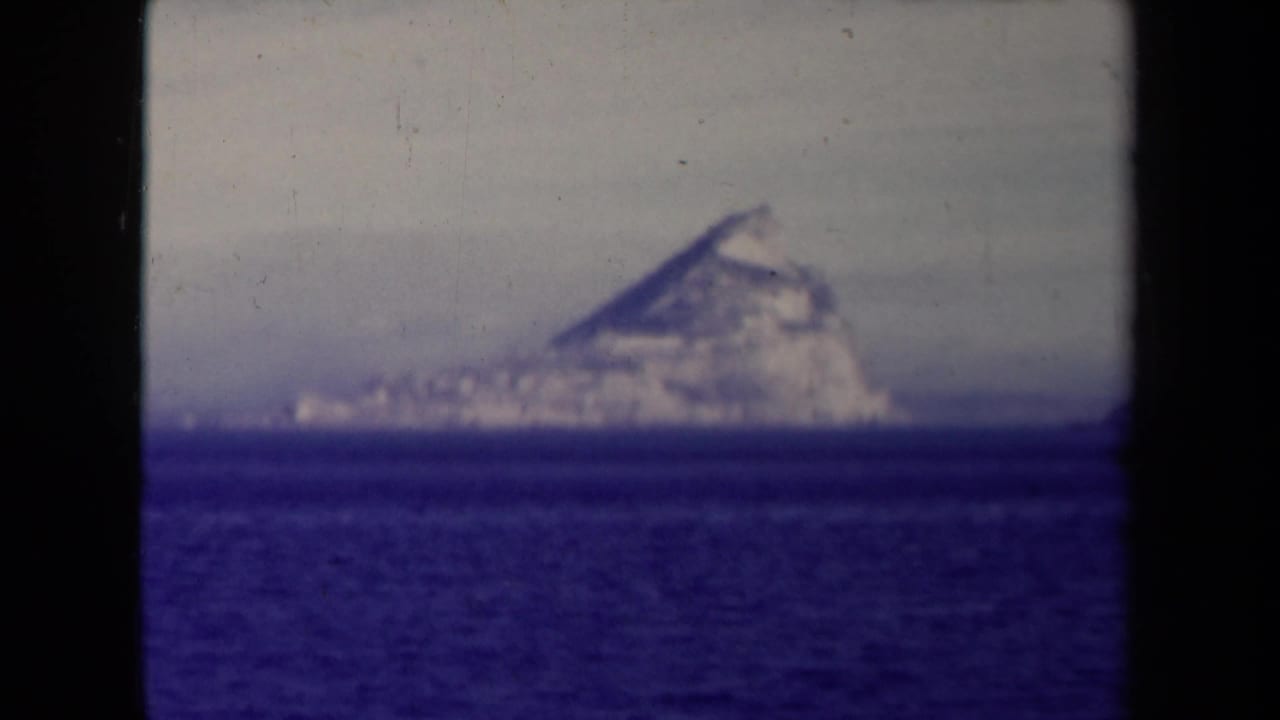 Rugged island or headland sits on the horizon beyond a band of blue sea.