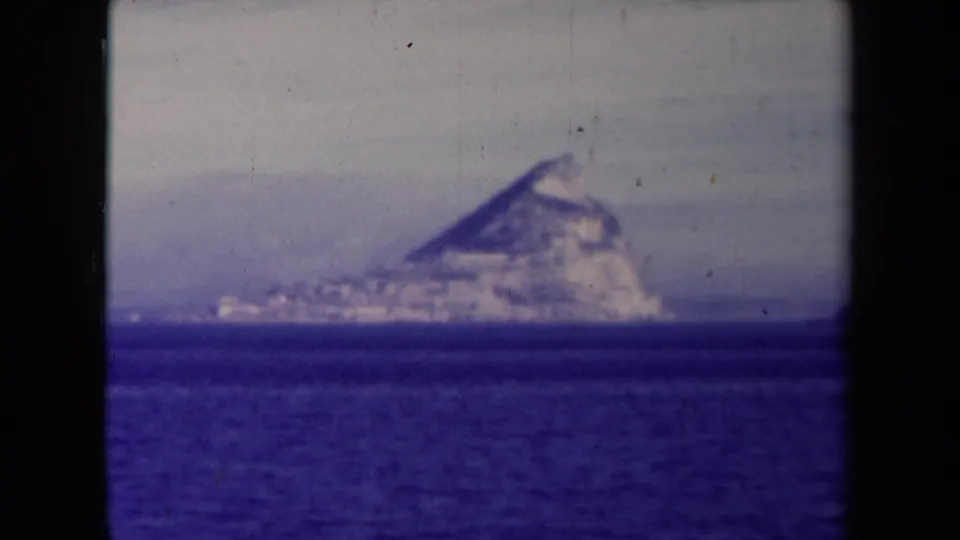 Final 1945 8mm frame holding on a distant rugged island or headland across the ocean, with dark borders and visible film wear.