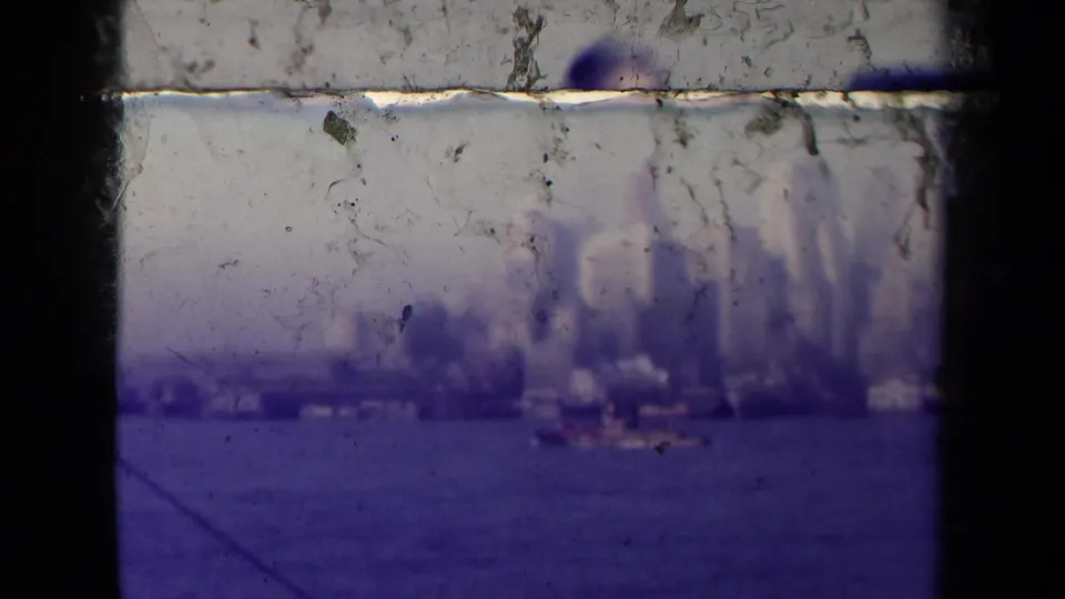 Soft 1945 France 8mm view of a distant waterfront skyline across open water with heavy scratches and dark gate edges.
