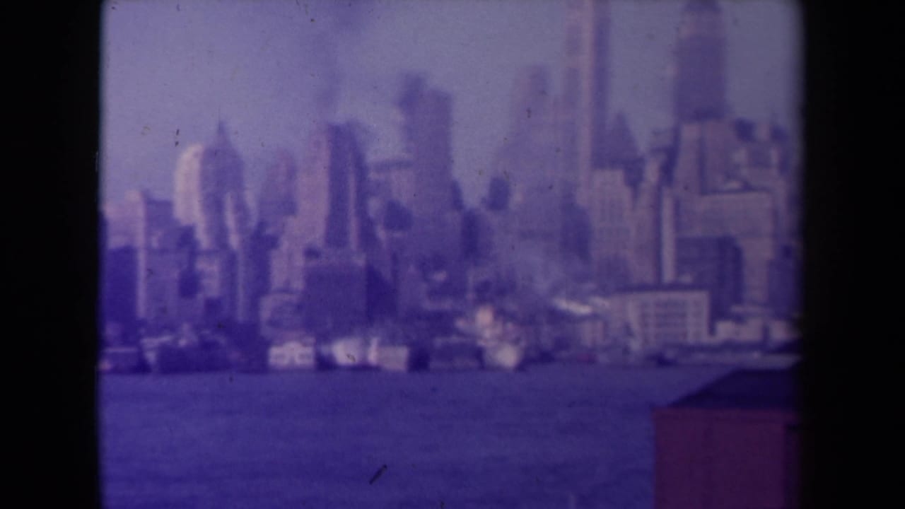 Hazy distant city skyline across water, framed by dark film borders.
