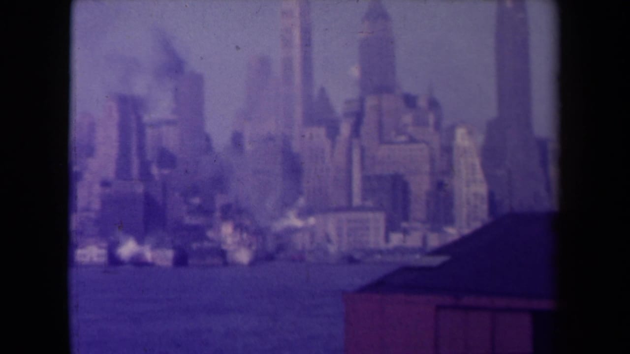 Blurred waterfront skyline with tall buildings and a dark roof at lower right.