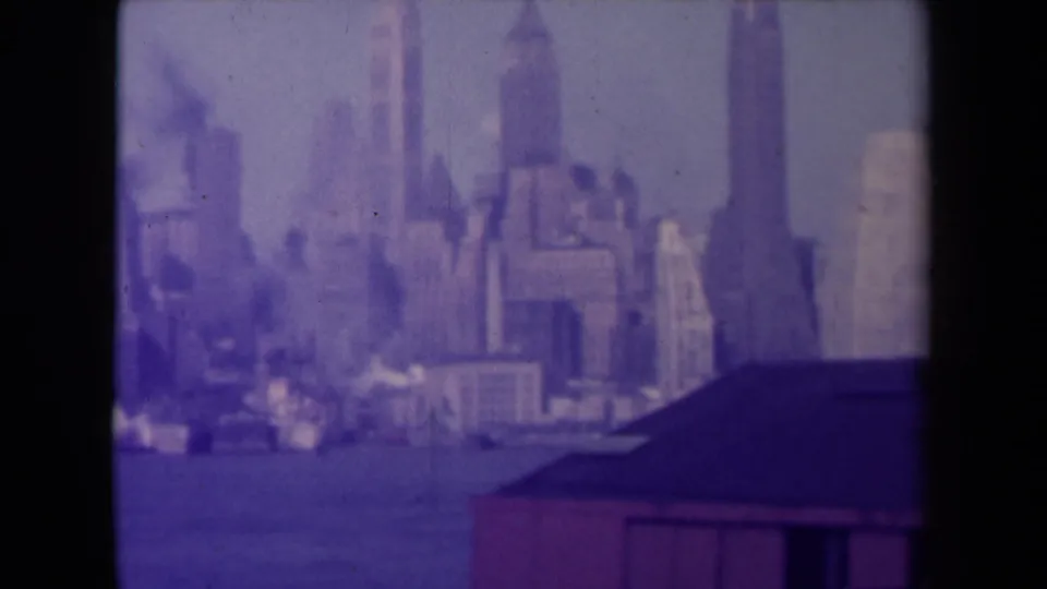 Purple-tinted 1940s skyline view across water, with soft focus, scratches, and dark edge framing.