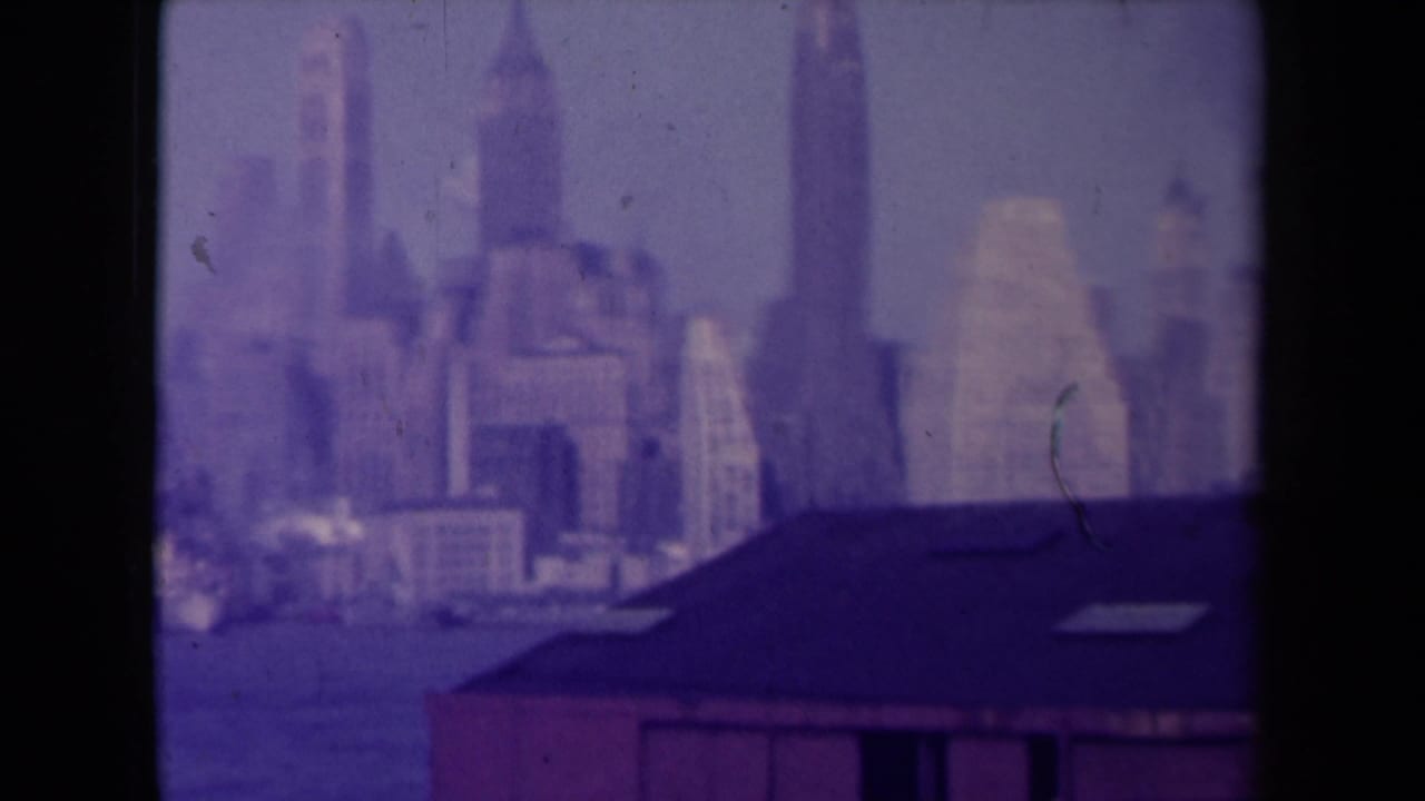 Hazy city skyline beyond a dark foreground roof, seen through purple-tinted film grain.
